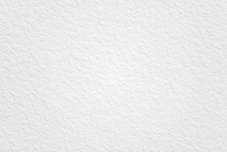 A textured white surface with uneven patterns and subtle variations in shading. The overall appearance is clean and minimalistic, with no distinct shapes or objects visible.