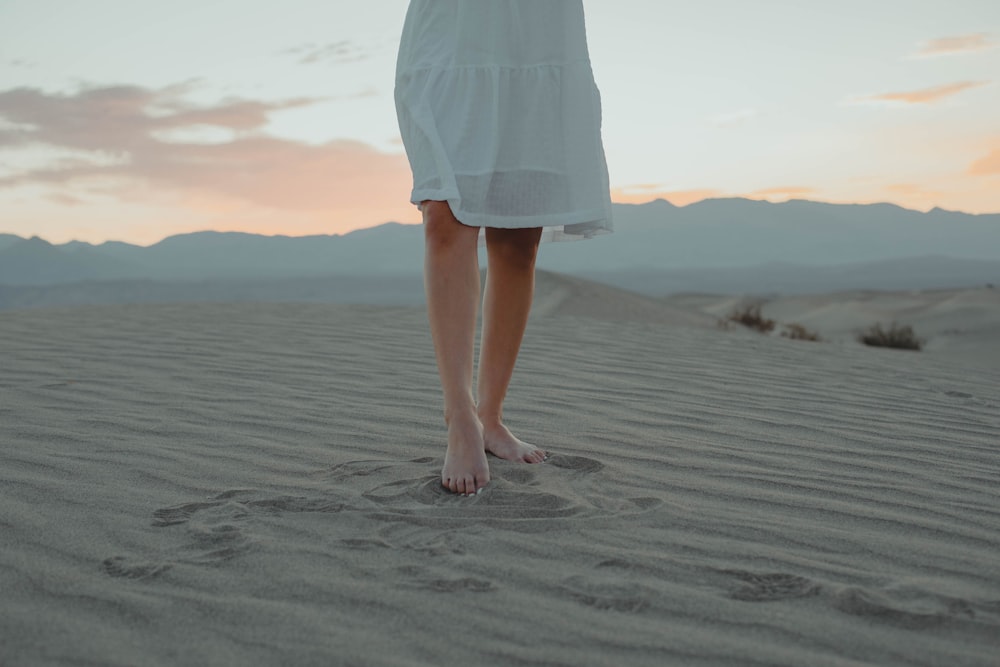 a woman in a white dress walking across a desert