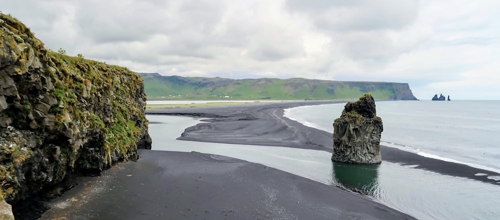 a black sand beach with a rock formation in the water