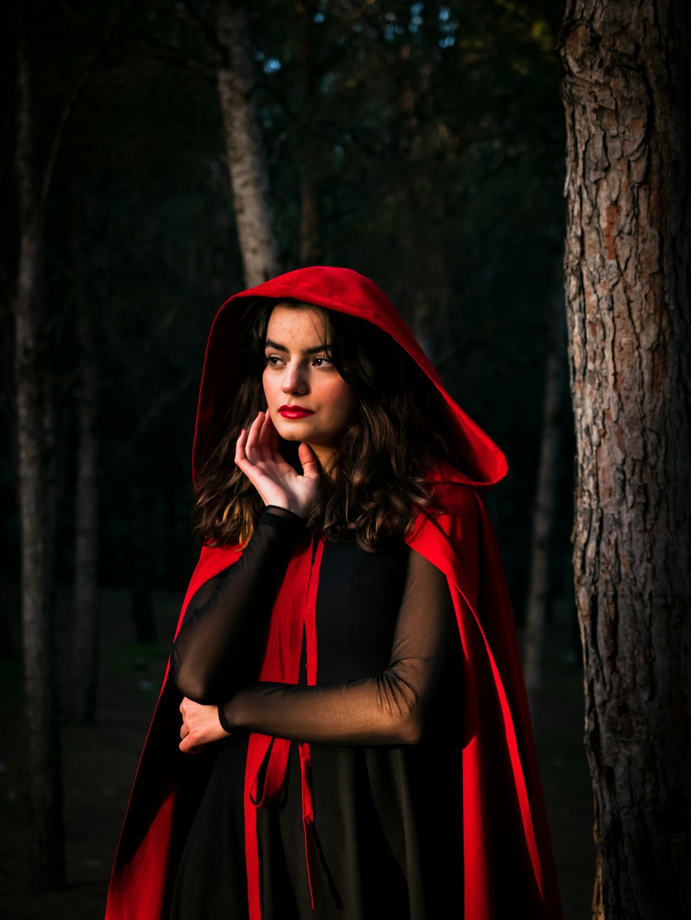 a woman in a red cape standing in the woods