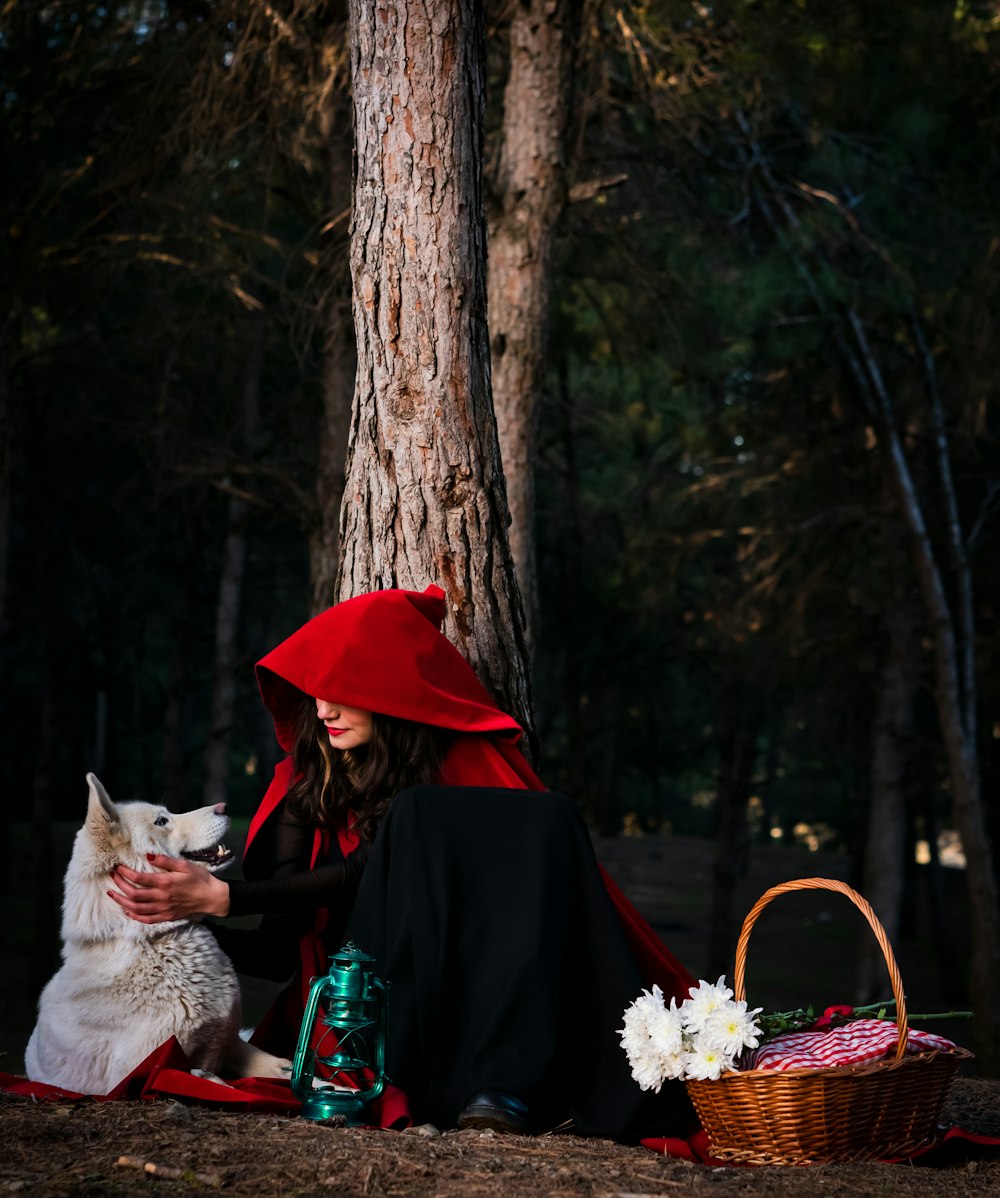 a woman in a red cloak sitting next to a white dog