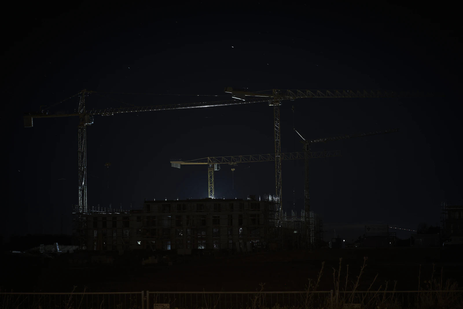 Construction site with tower cranes at night behind perimeter fencing