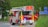 A red and yellow fire truck is positioned on a road near some grass and shrubbery, with signs pointing towards Berlin and Braunschweig. The truck is equipped with a ladder and marked with 'Feuerwehr' indicating it's part of the fire brigade. Traffic cones are placed near the truck.