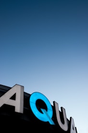 Large illuminated signage displaying the letters 'AQUA' against the backdrop of a clear gradient sky transitioning from deep blue to lighter blue near the horizon.