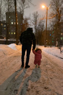 a man walking down a snow covered street holding a small child's hand