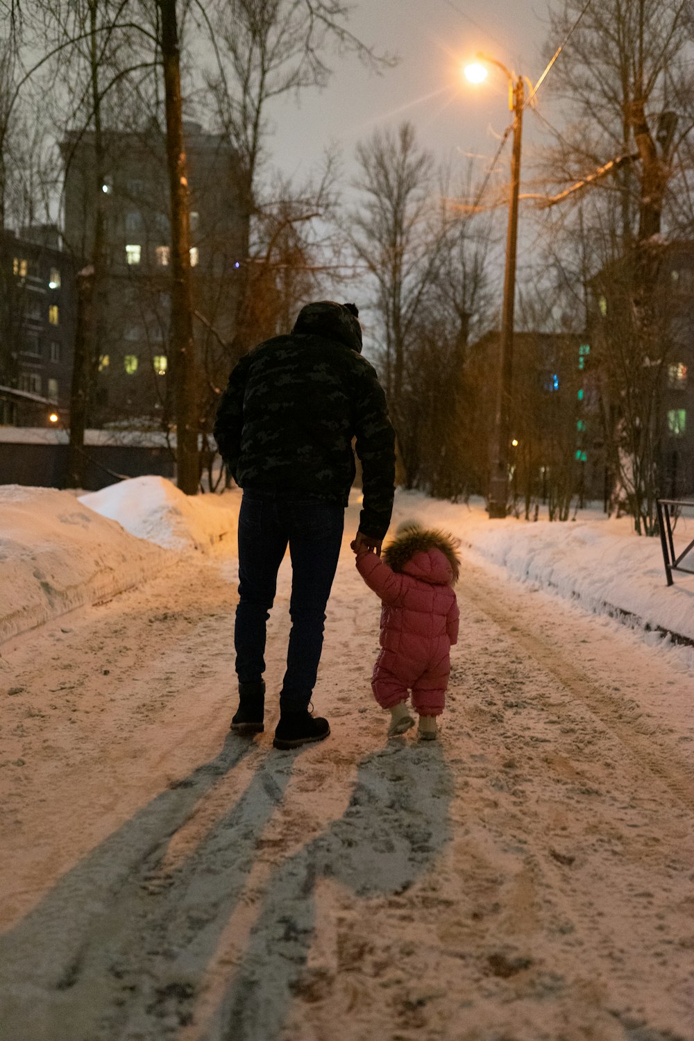 a man walking down a snow covered street holding a small child's hand