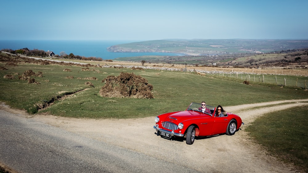 a red convertible car driving down a dirt road