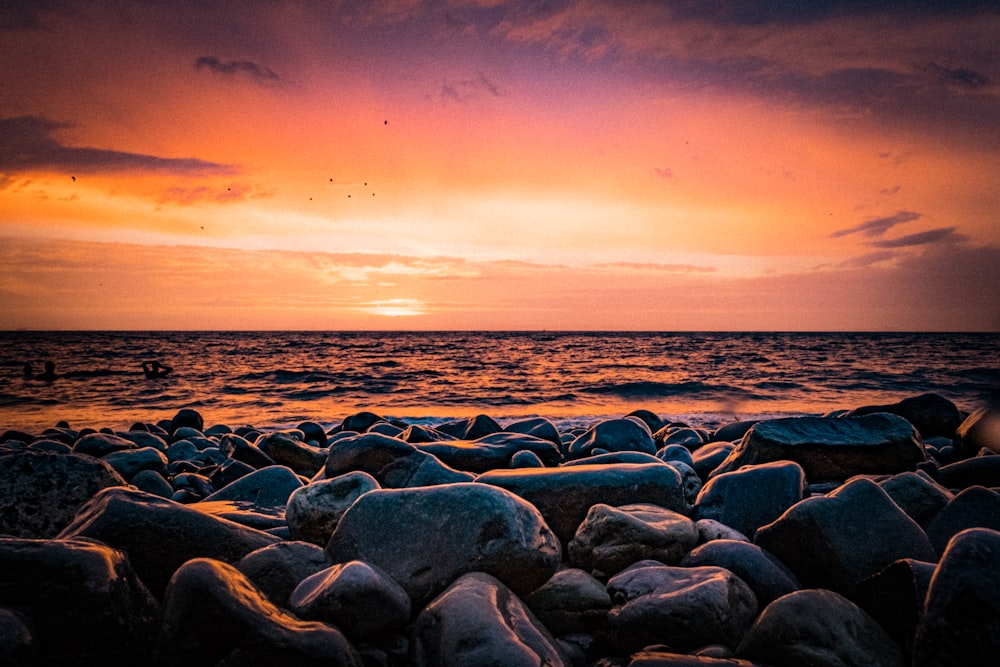 the sun is setting over the ocean and rocks