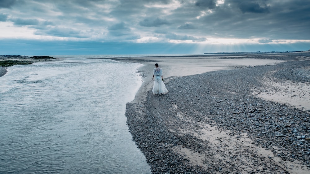 a woman in a white dress walking along a beach