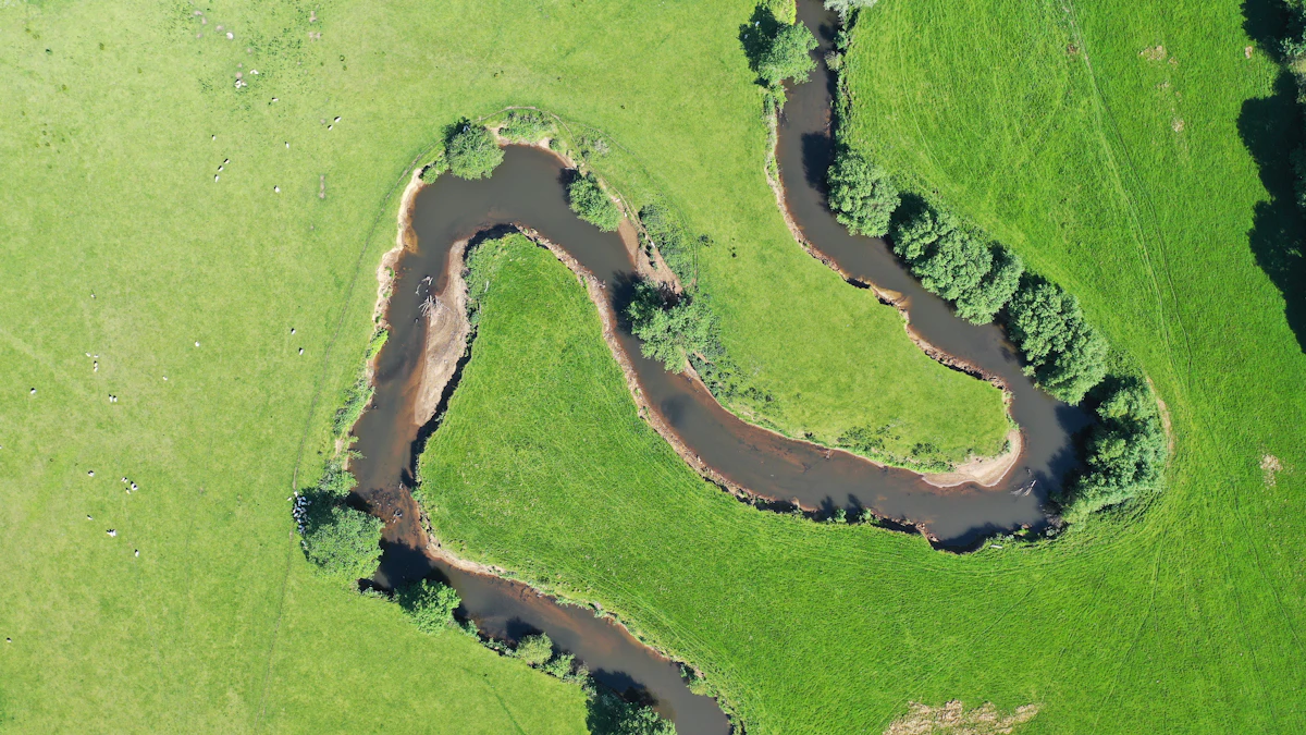 Aerial view of a meandering river cutting through pasture — the outer-bend cutbanks where Texas Tuff Rock Bags interrupt meander migration