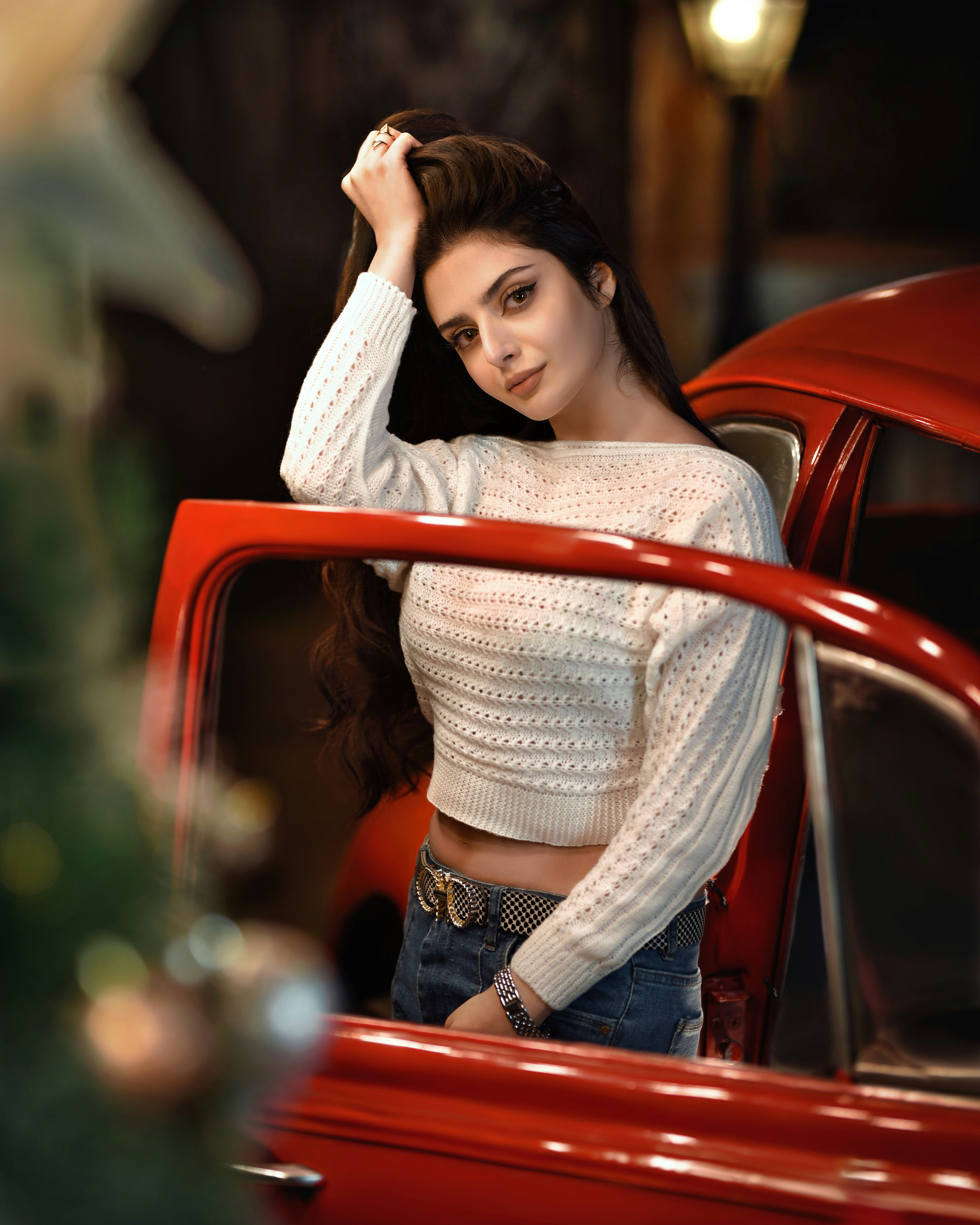 a young woman leaning on the hood of a red car