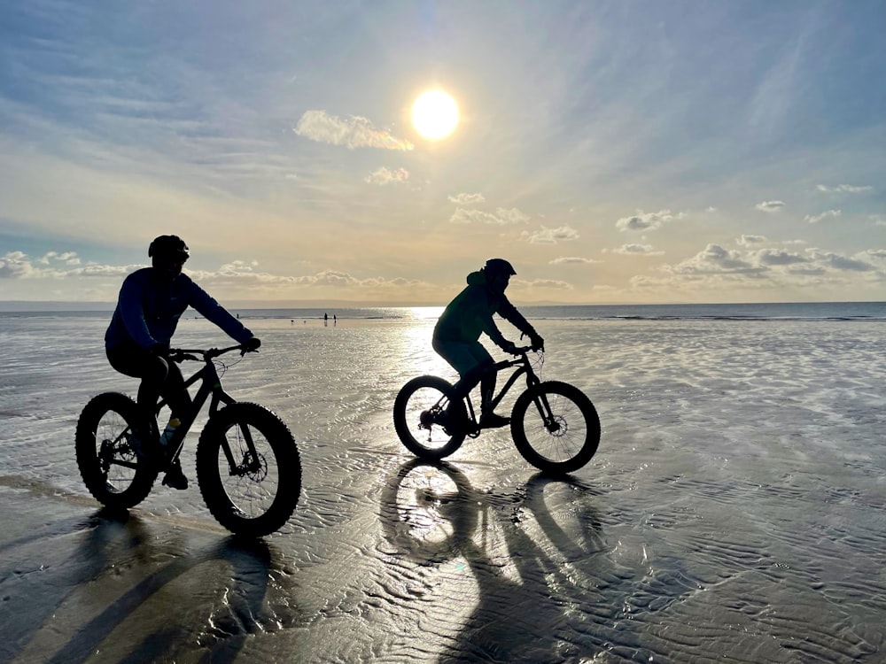 a couple of people riding bikes on top of a beach