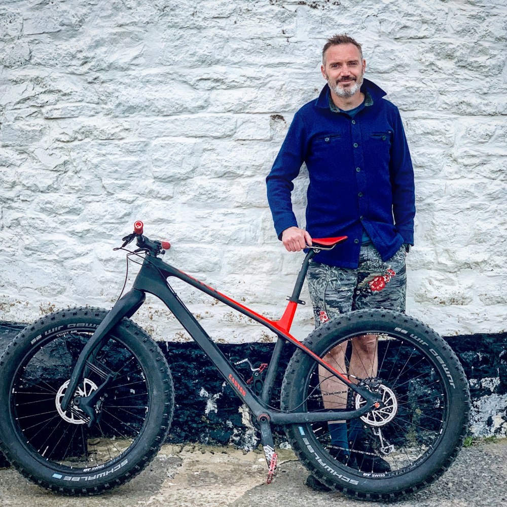 a man standing next to a bike in front of a white wall