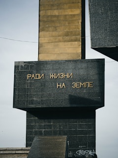 A monument featuring a tall, rectangular structure with a large stone base. The structure has golden text in Russian that translates to 'For Life on Earth.' The material appears to be a combination of dark stone and metal.