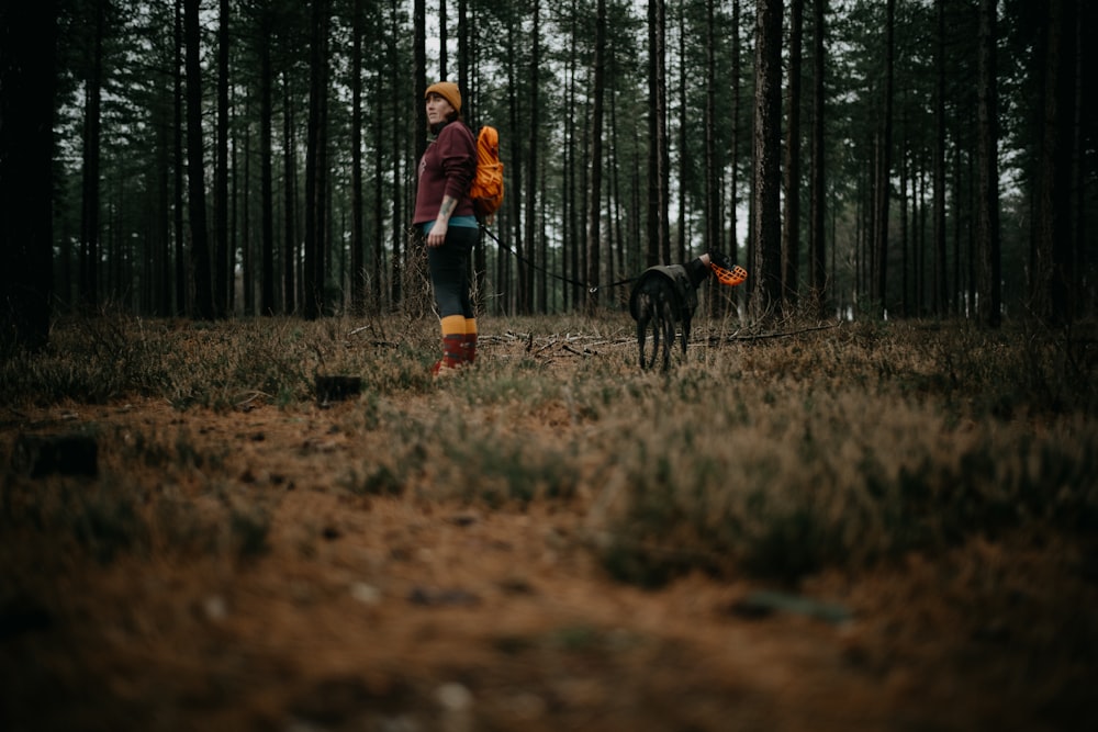 a woman with a backpack and a dog in the woods