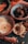 An assortment of dried fruits and nuts is arranged in decorative bowls and scattered on a dark surface. The bowls contain dried apricots, pistachios, and slices of dried pineapple. The intricate patterns on the bowls add an artistic touch to the rustic presentation.