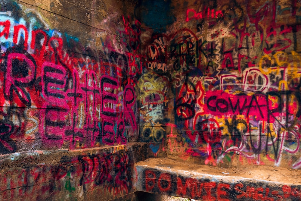 a wall covered in lots of graffiti next to a bench