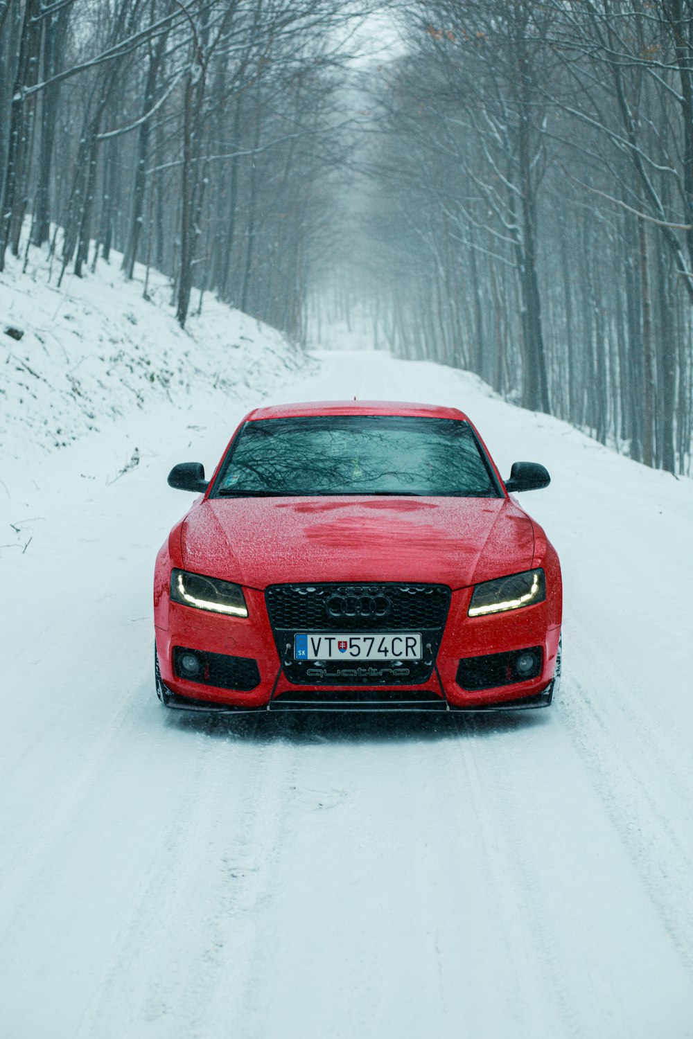 a red car driving down a snow covered road