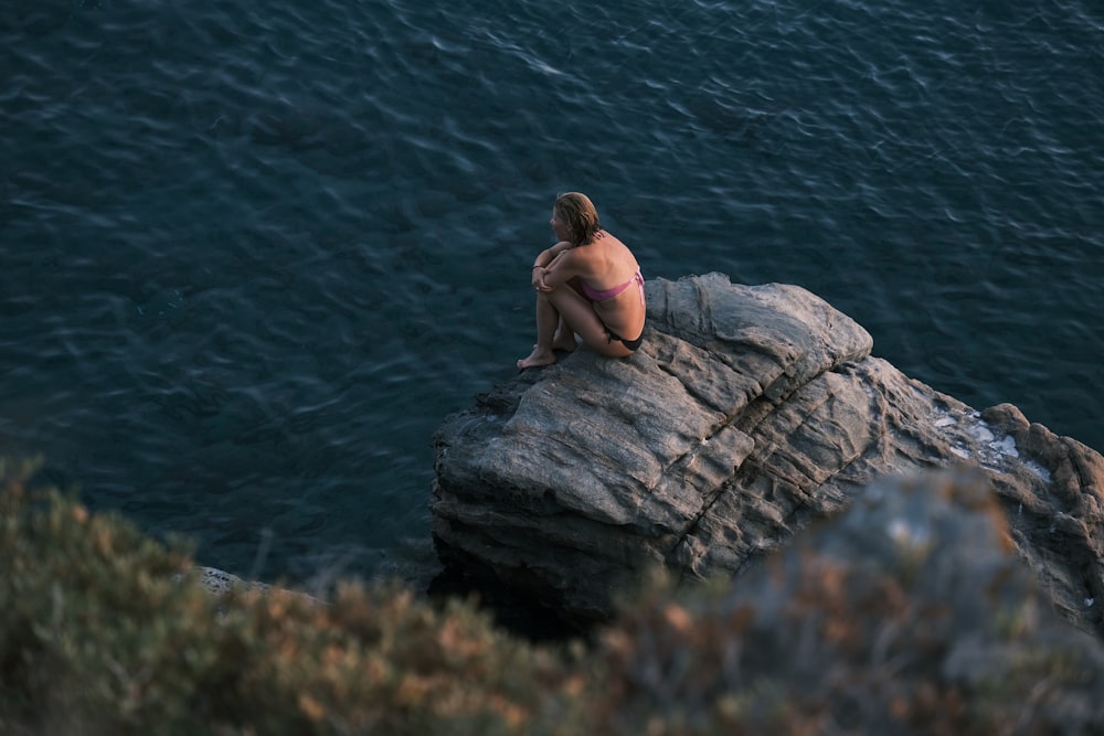 Una donna in bikini seduta sulla cima di una roccia