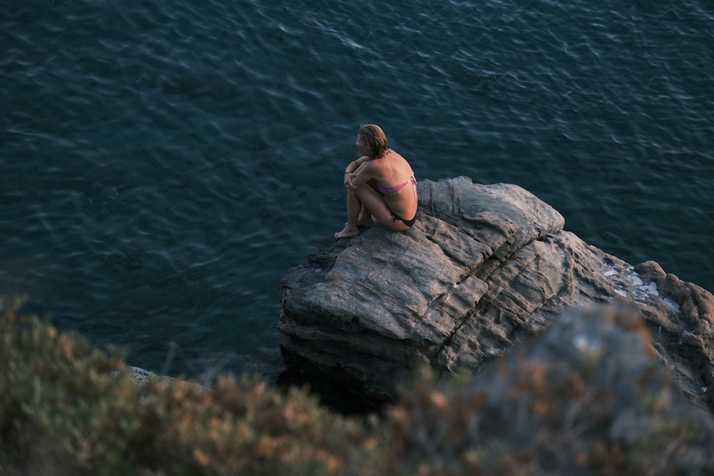 Une femme en bikini assise au sommet d’un rocher