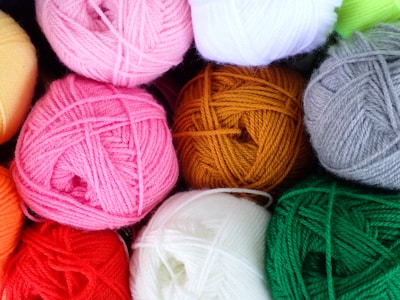 A close-up view of multiple skeins of yarn in an assortment of colors, neatly arranged and overlapping each other. The yarn is tightly wound, showcasing its soft texture and vibrant hues.