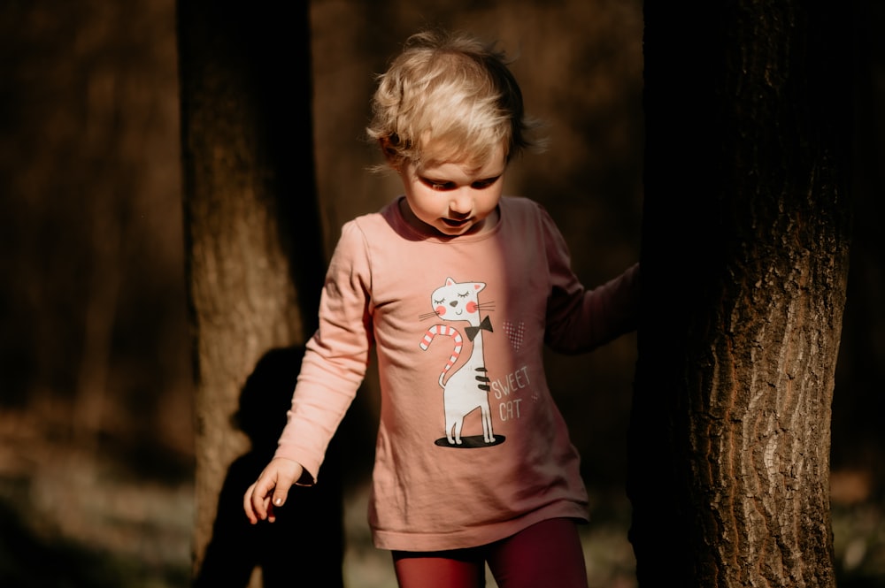 a little girl standing next to a tree