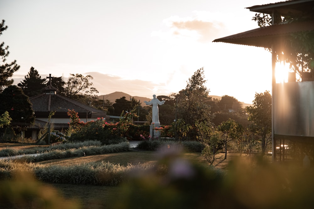 the sun is setting behind a statue in a garden