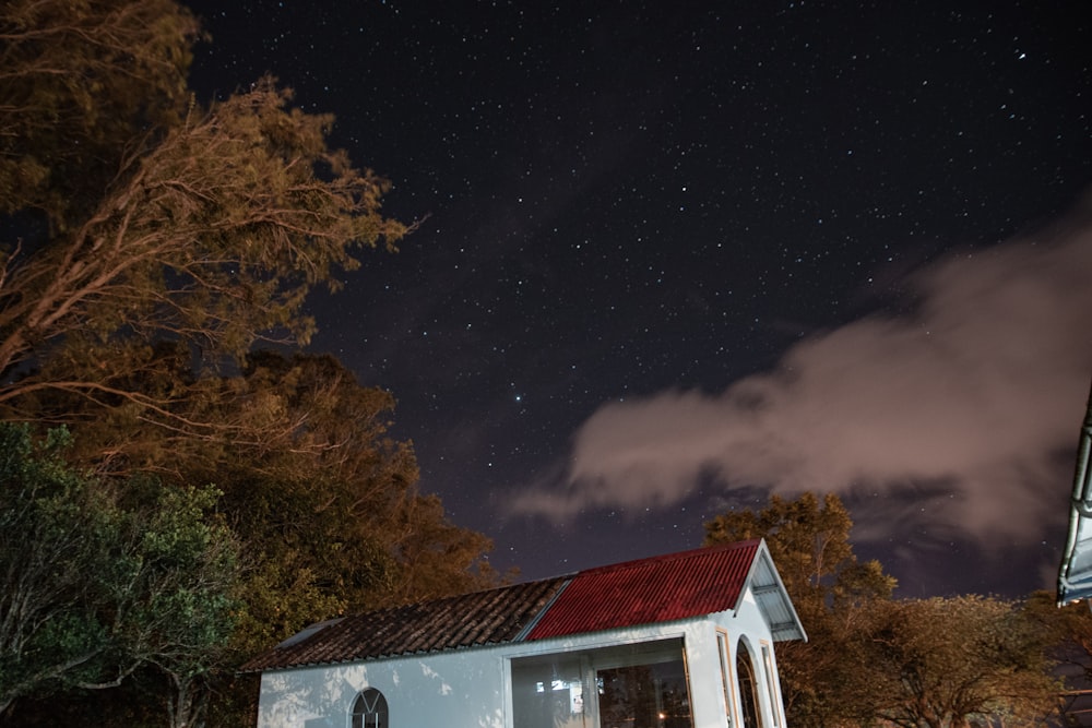 a small white building with a red roof under a night sky