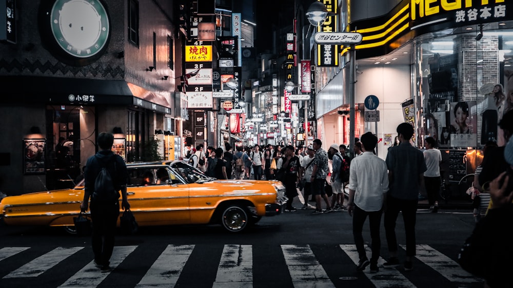um grupo de pessoas andando através de uma rua ao lado de um carro amarelo