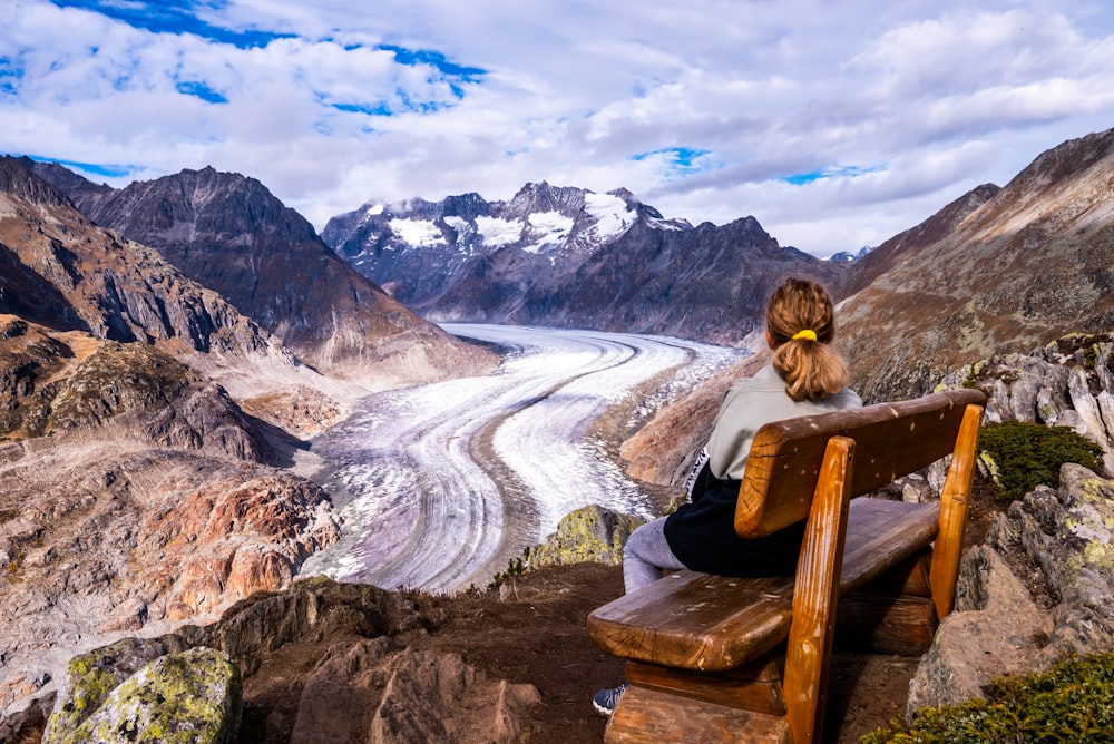 a woman sitting on a bench looking at a glacier