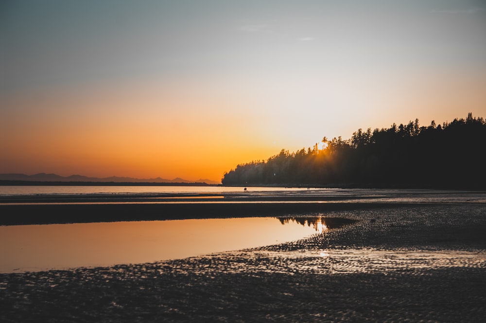 the sun is setting over the water at the beach