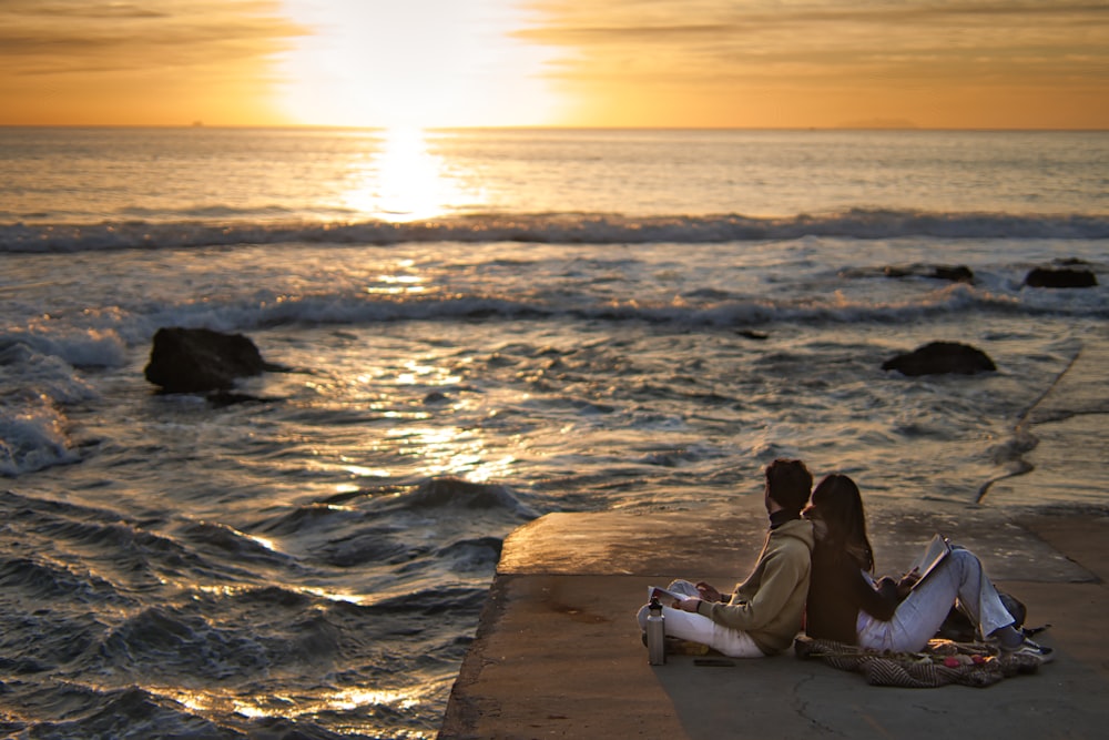 a couple of people sitting on top of a pier next to the ocean