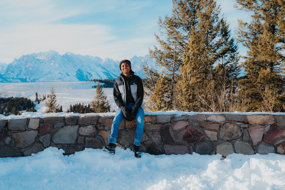 a man sitting on a stone wall in the snow