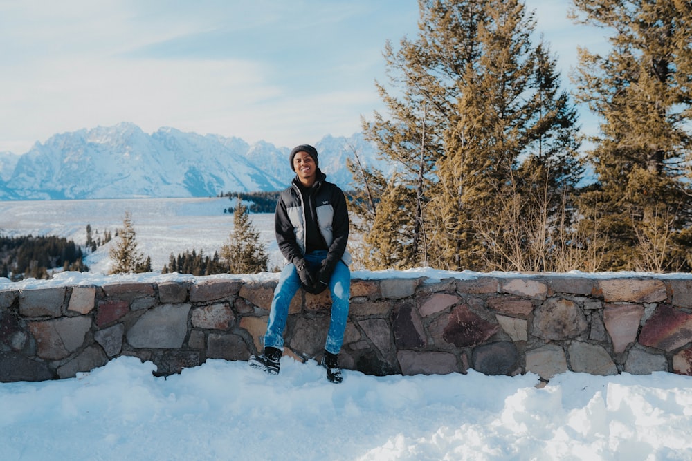 a man sitting on a stone wall in the snow