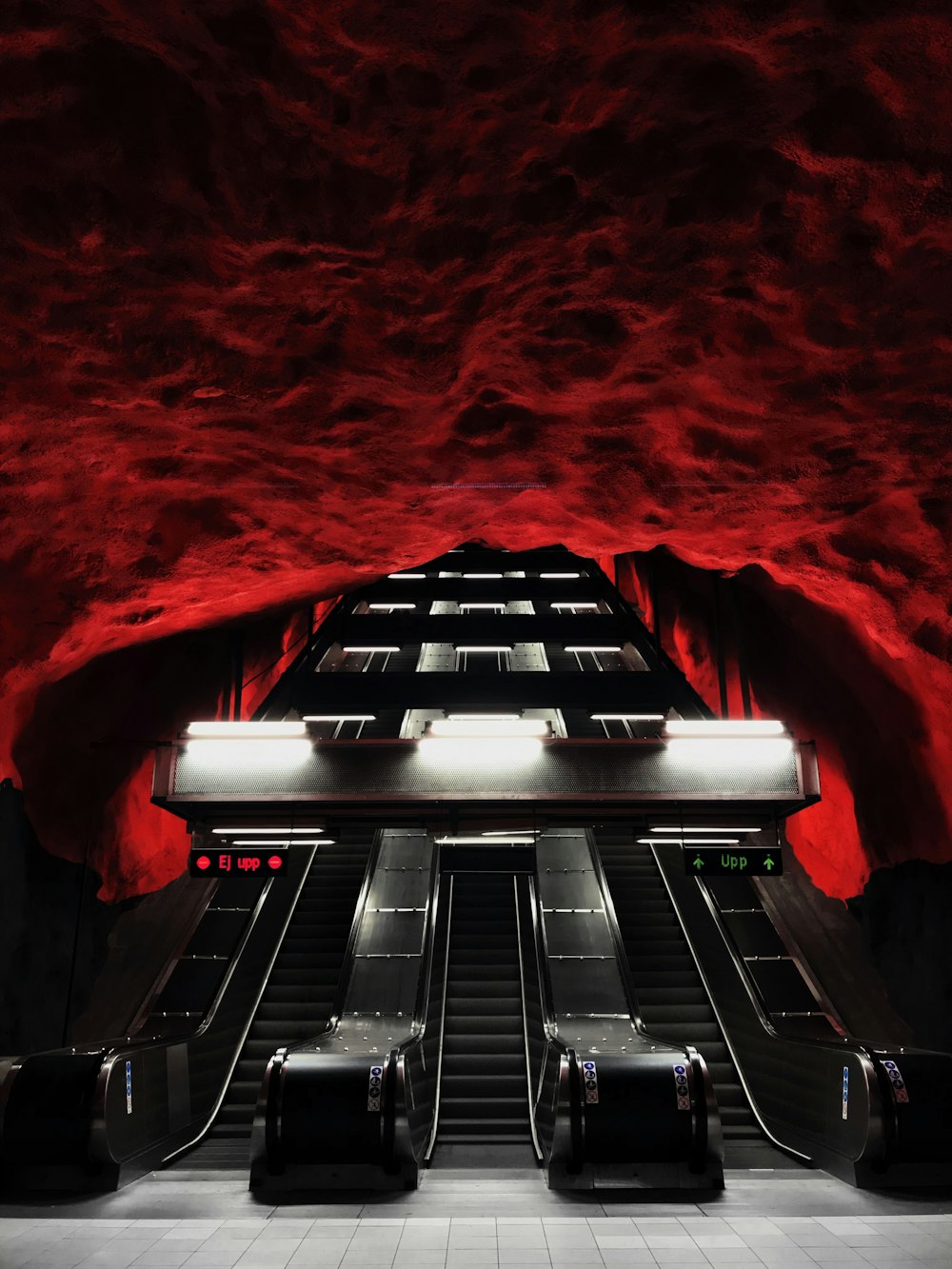 uma escada rolante em uma estação de metrô com paredes vermelhas