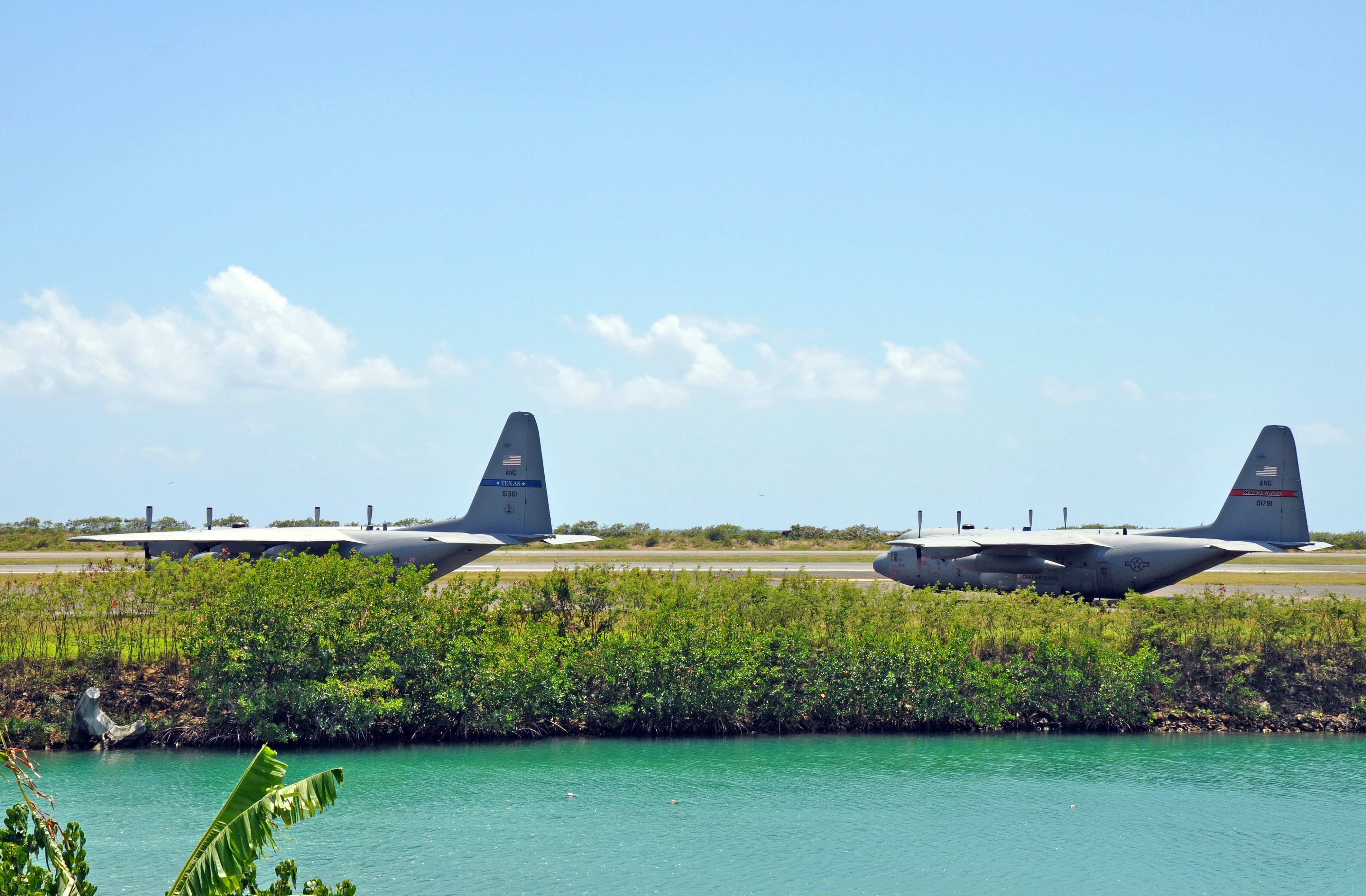 Air National Guard C130s from Texas and Mansfield, Ohio sit on an airport tarmac next to the sea.