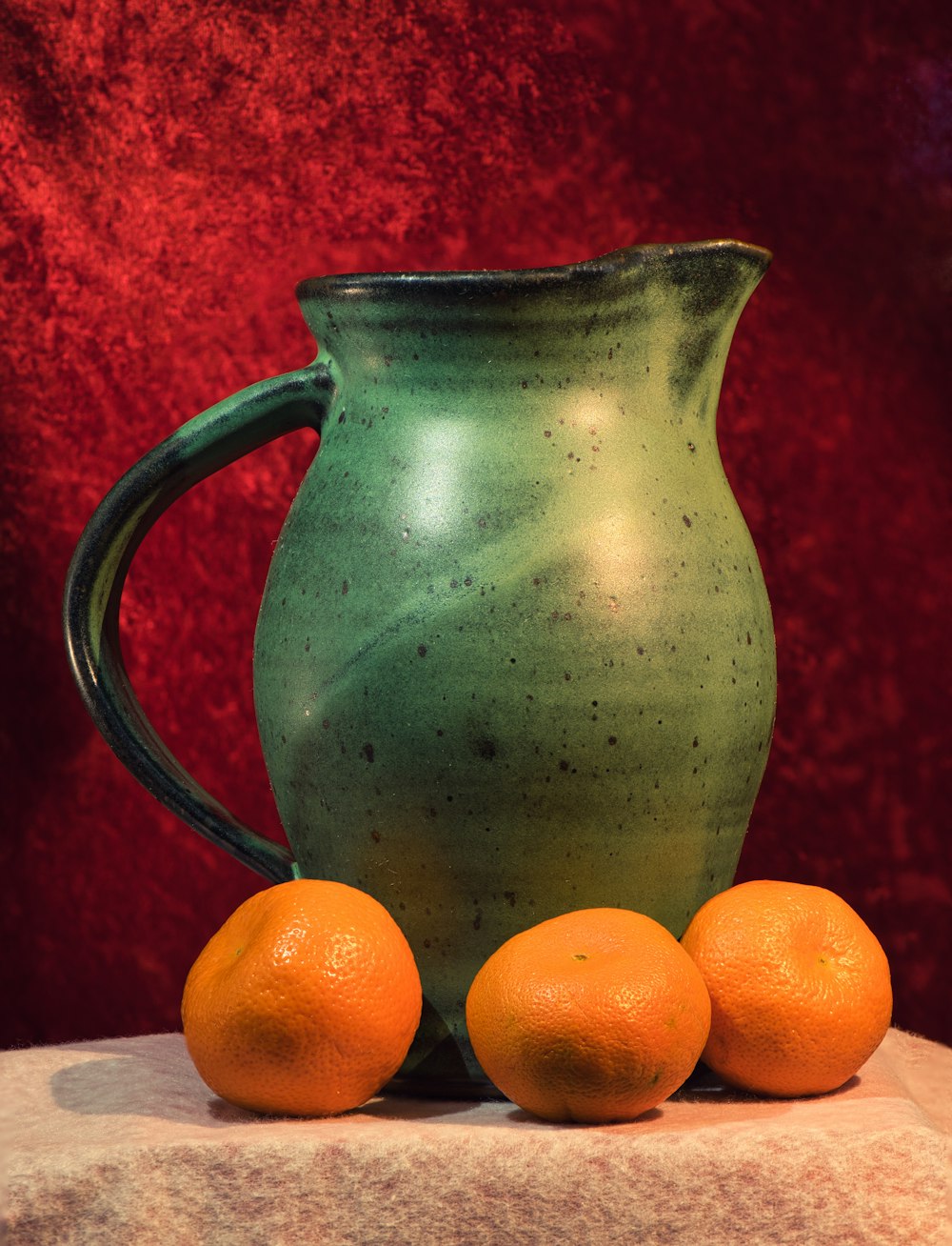 a green pitcher sitting on top of a table next to three oranges