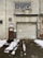 A weathered industrial building features a large, rolled-down metal garage door next to a smaller, rusted brown door with official signage. Above the garage door, there is a rectangular window with an air conditioning unit installed. Snow patches cover the ground in front, creating a stark contrast against the dark, wet pavement.