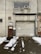 A weathered industrial building features a large, rolled-down metal garage door next to a smaller, rusted brown door with official signage. Above the garage door, there is a rectangular window with an air conditioning unit installed. Snow patches cover the ground in front, creating a stark contrast against the dark, wet pavement.
