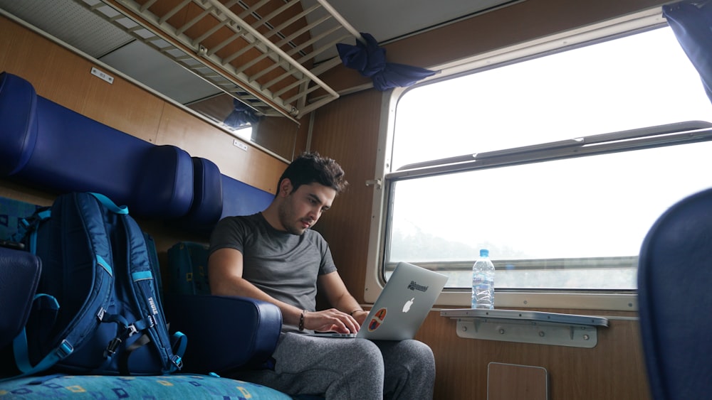 a man sitting on a train looking at his laptop