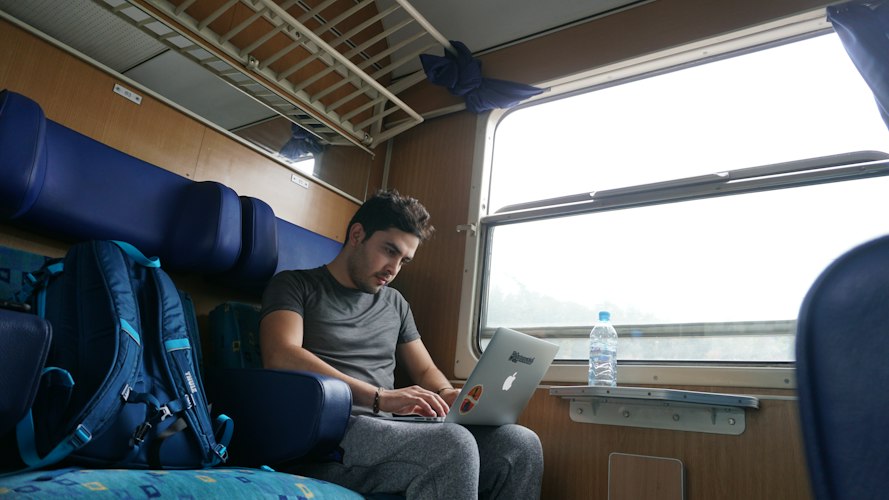 Traveler typing notes on a laptop at a café table with a scenic view in the background