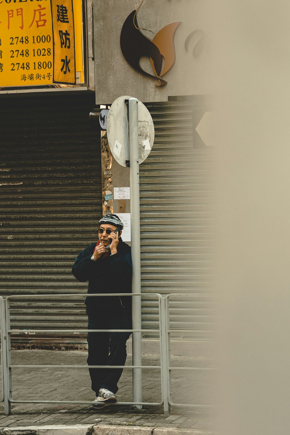 a man standing next to a street sign talking on a cell phone