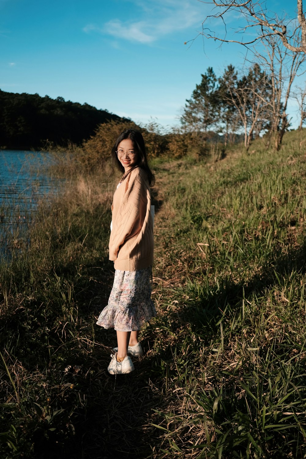 a little girl standing in a field next to a body of water