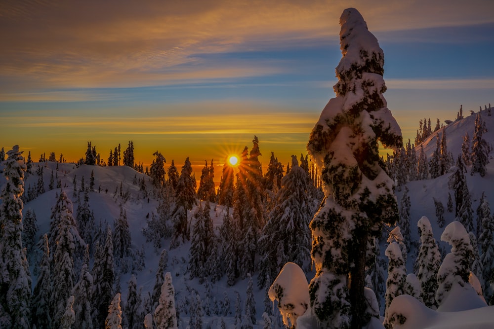 the sun is setting over a snowy mountain