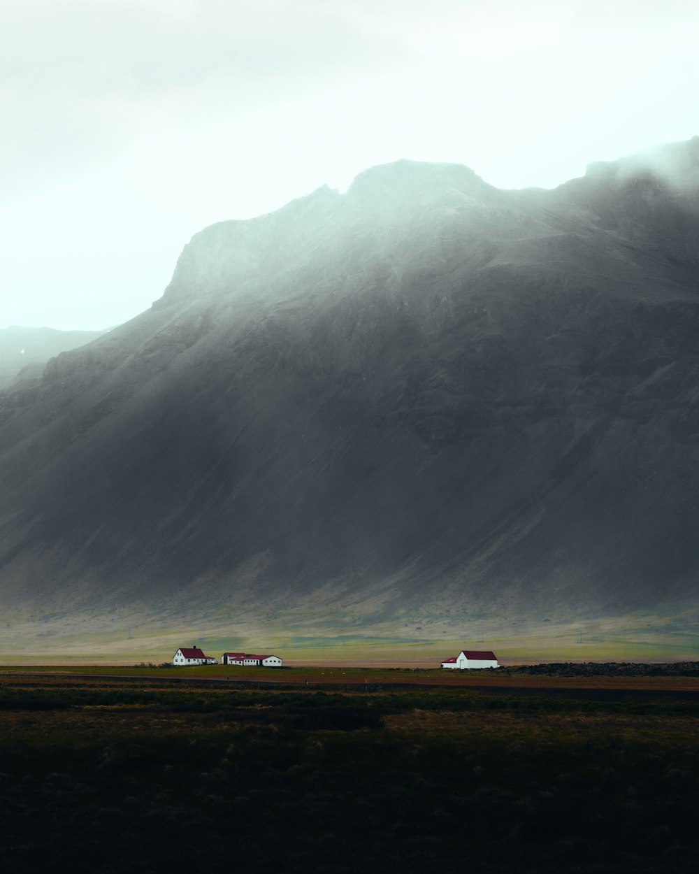 a large mountain with a few houses in the foreground