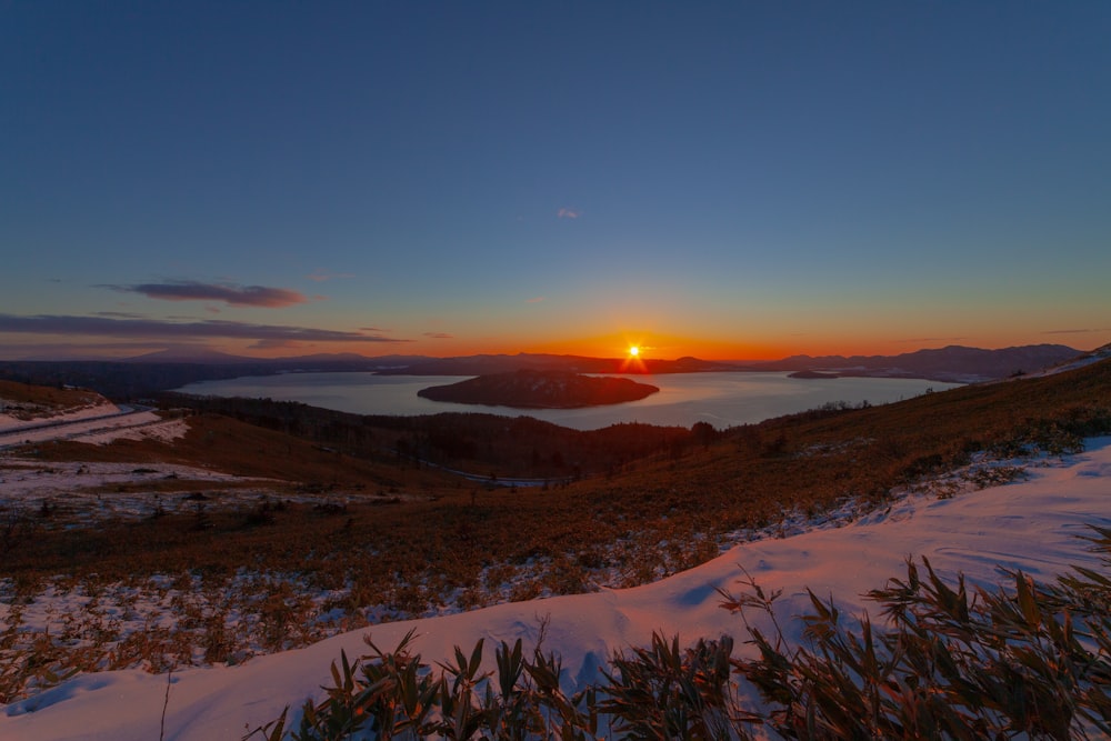 the sun is setting over a snowy hill