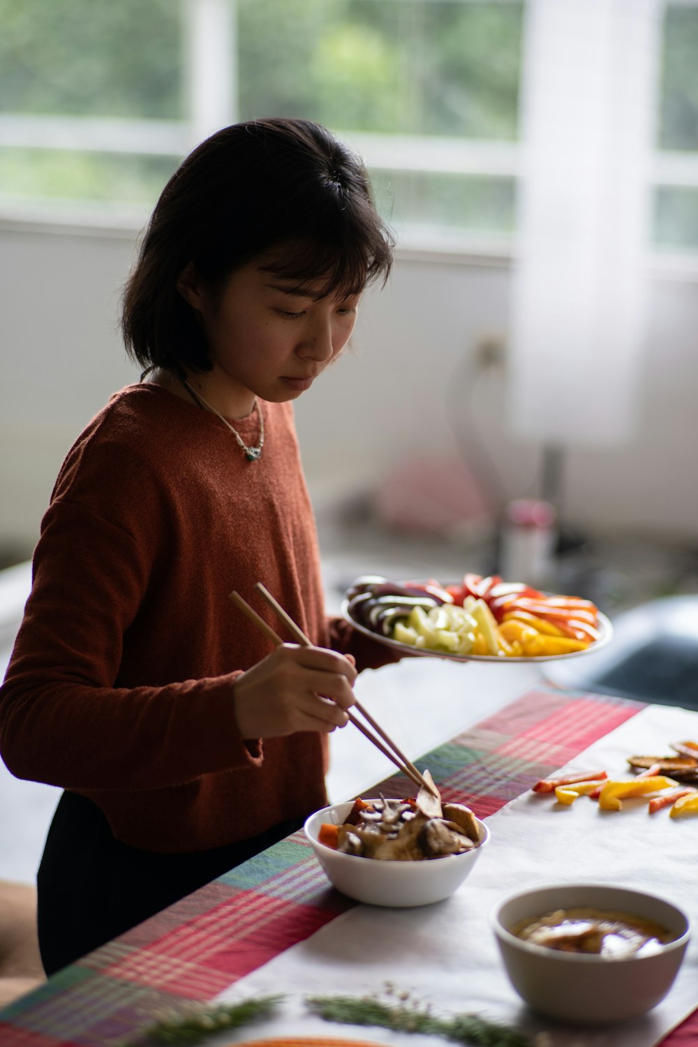 a woman holding a plate of food with chopsticks