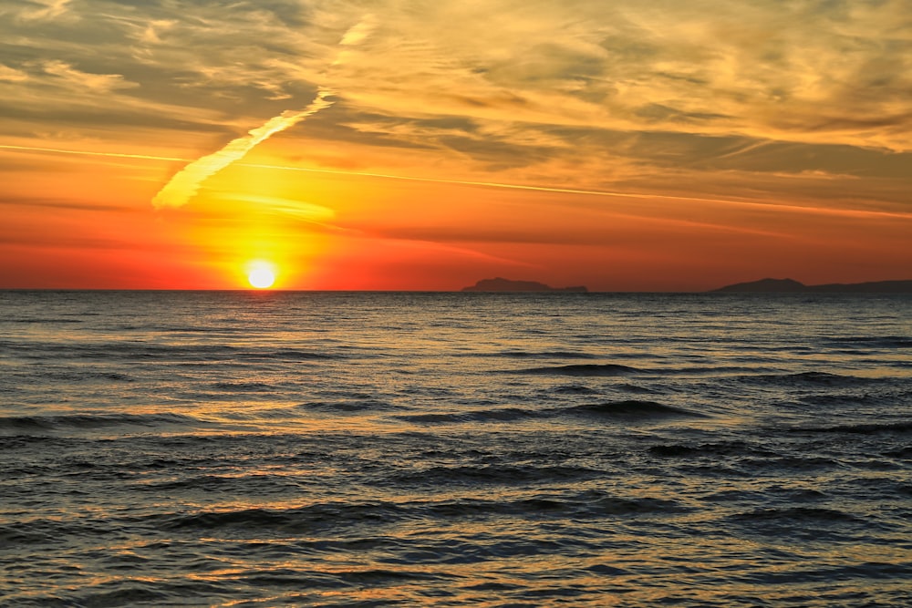 a sunset over a body of water with mountains in the distance