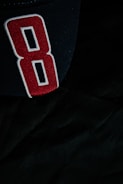 A black fabric surface with a large, embroidered number 8 designed in red with white and black outlines.