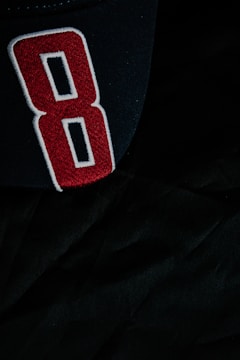 A black fabric surface with a large, embroidered number 8 designed in red with white and black outlines.